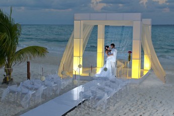 bride and groom under lit pergola on the beach